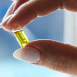 Closeup of a hand holding a cannabis capsule in front of a window.