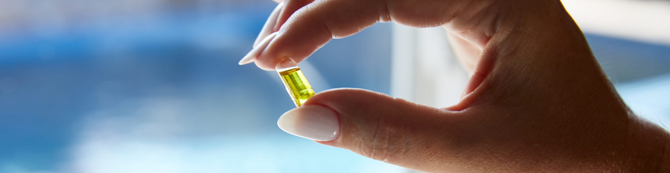 Closeup of a hand holding a cannabis capsule in front of a window.