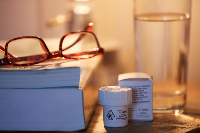 Cannabis capsule bottle, glass of water, and books on nightstand.