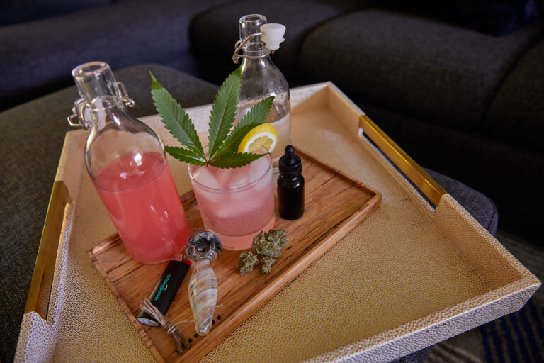 Click to see a larger version of the image Cannabis infused cocktail and pitcher surrounded by cannabis flower and smoking accessories.
