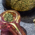Cannabis, pink pipe, and hemp wick on marble countertop.