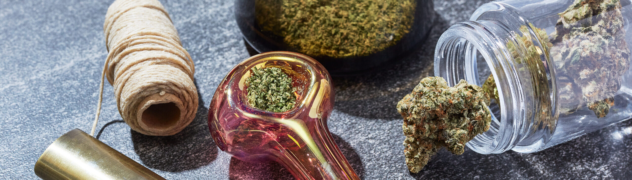 Cannabis, pink pipe, and hemp wick on marble countertop.