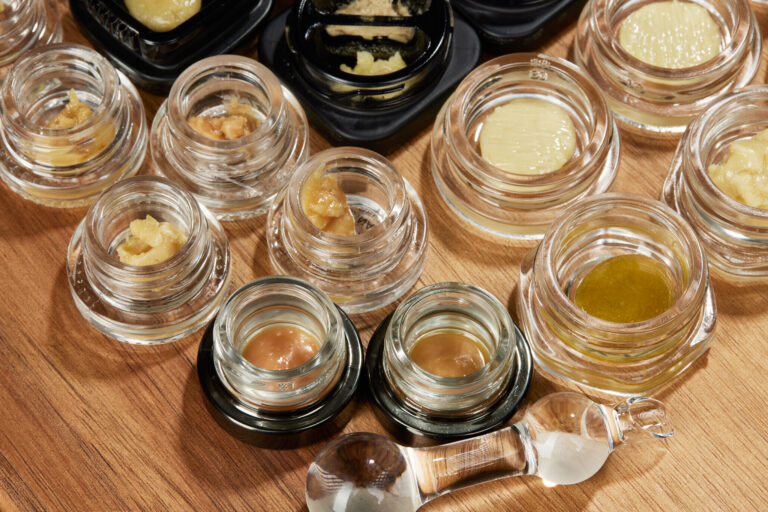 Top down shot of various cannabis concentrates in jars on wood table.