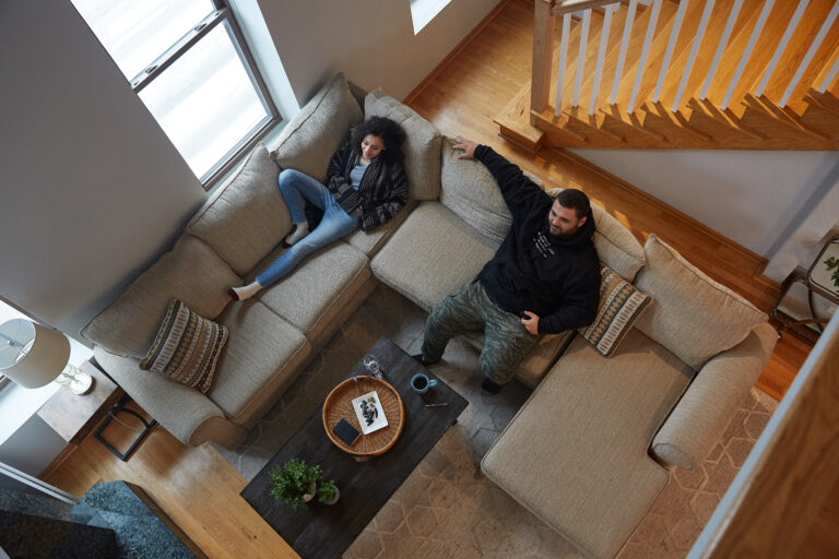 Click to see a larger version of the image Top-down image of two people hanging out on tan couch.
