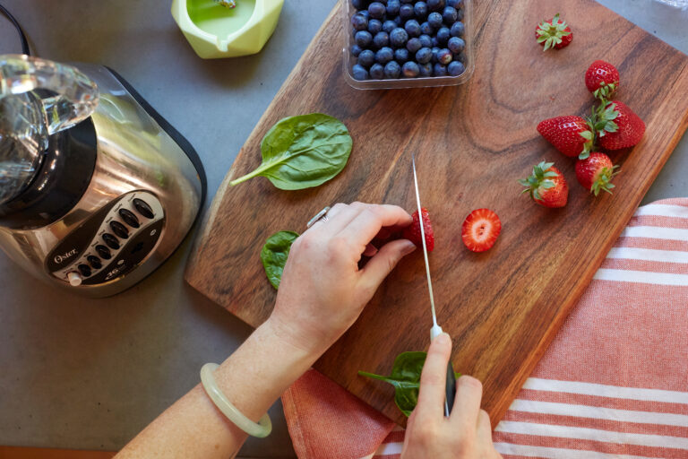 Click to see a larger version of the image Hands cutting strawberries on wooden cutting board.
