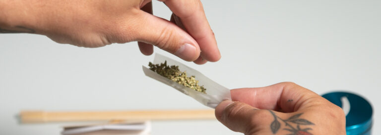 Close up of hands sprinkling ground cannabis into rolling paper.