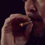 Closeup of man smoking joint on black background.