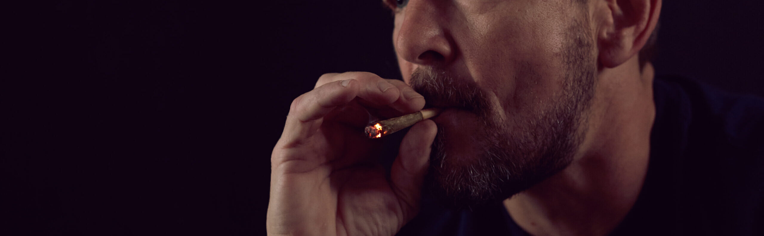 Closeup of man smoking joint on black background.
