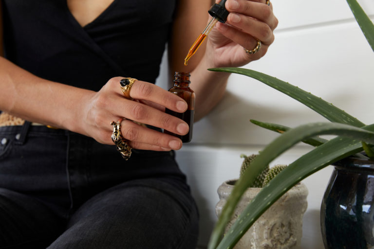 Click to see a larger version of the image Closeup of hands holding dropper and bottle of cannabis tincture.