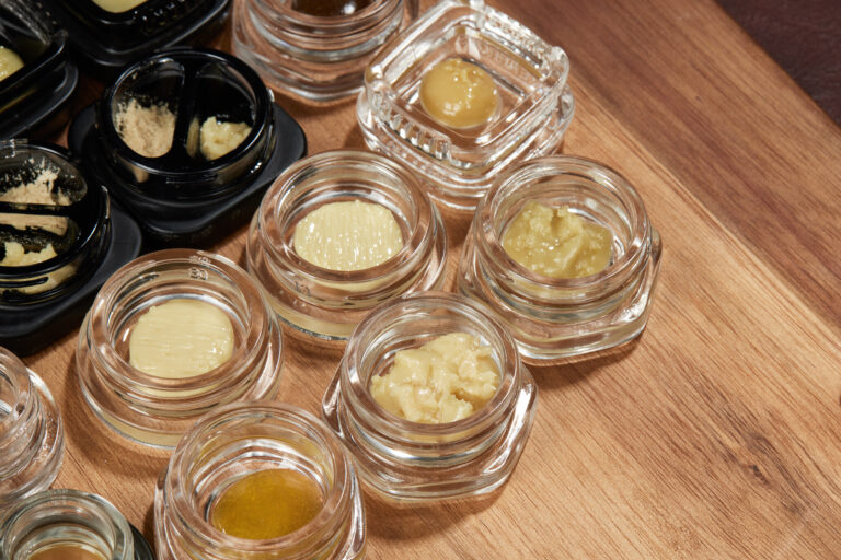 Click to see a larger version of the image Small jars filled with cannabis concentrates on wood table.