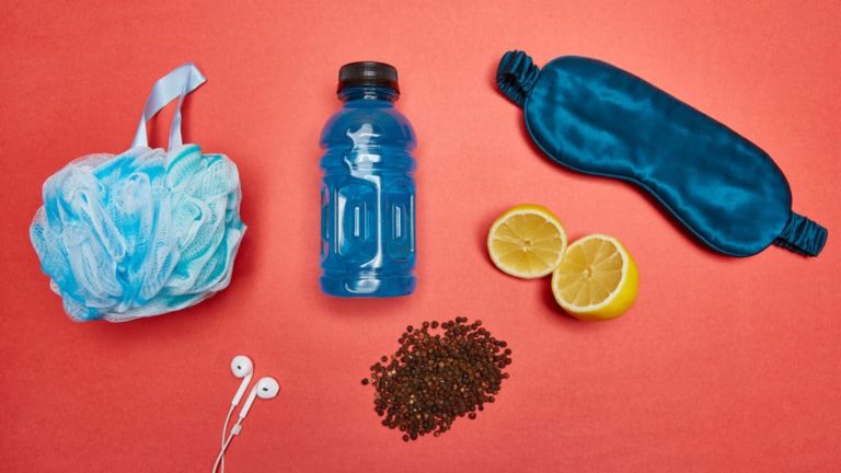 Various wellness items for detoxing: waterbottle, loofah, earbuds, sleep mask, lemon cut in half, and water bottle