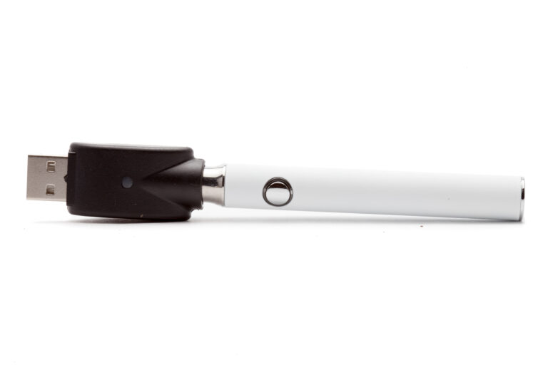 Click to see a larger version of the image White vape pen with charger on its side on white background.