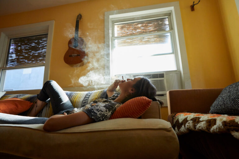 woman laying on a couch exhaling smoke from a joint