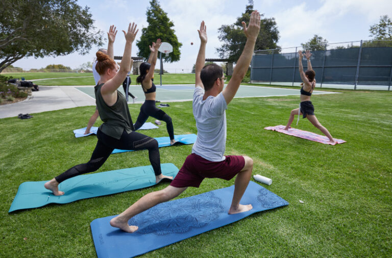 A group of people practicing yoga outside on a grassy area under clear skies.