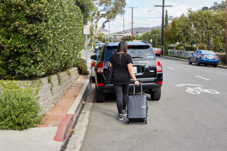 a woman pulling a rolling suitcase outside to a car
