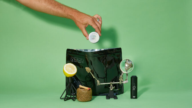 Hand pulling cannabis products out of small black bag on green background.