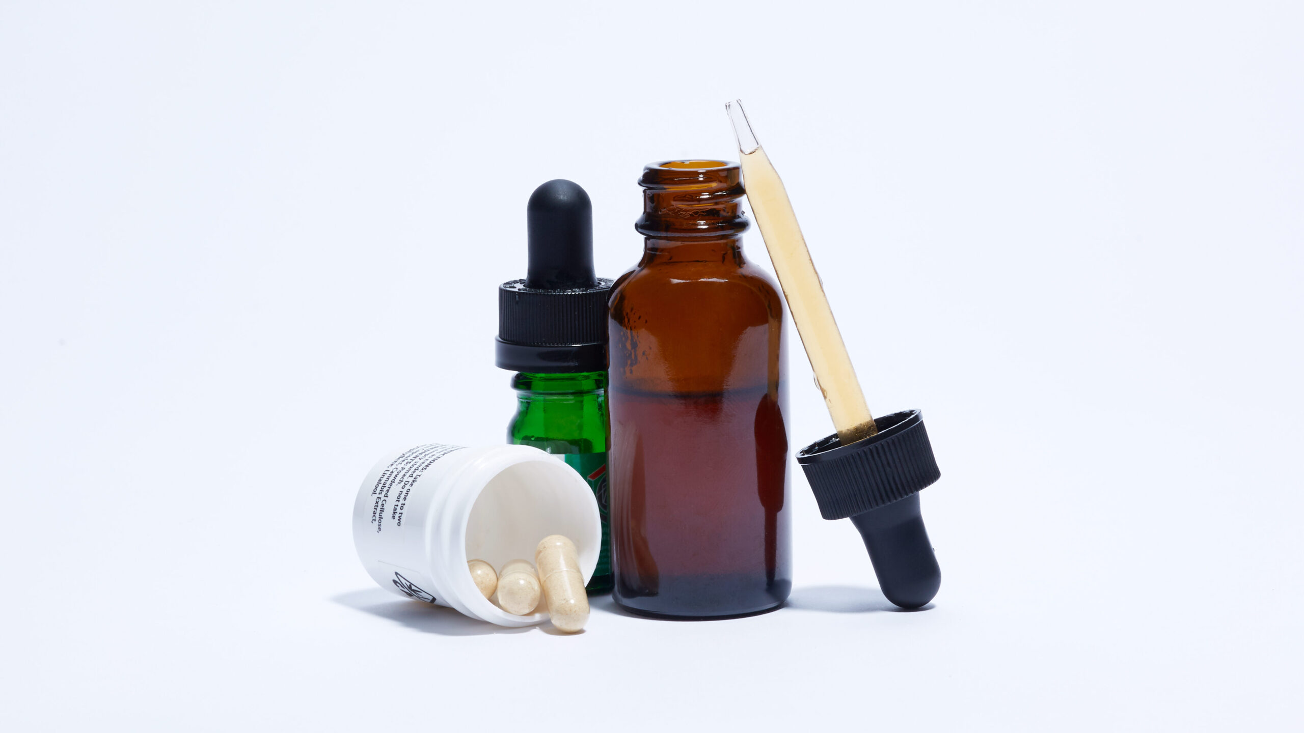 Tincture and cannabis capsule bottles on white background.