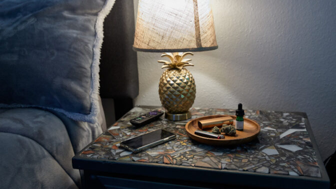 Weed, a pipe, and a phone on a tray on a nightstand with a lamp